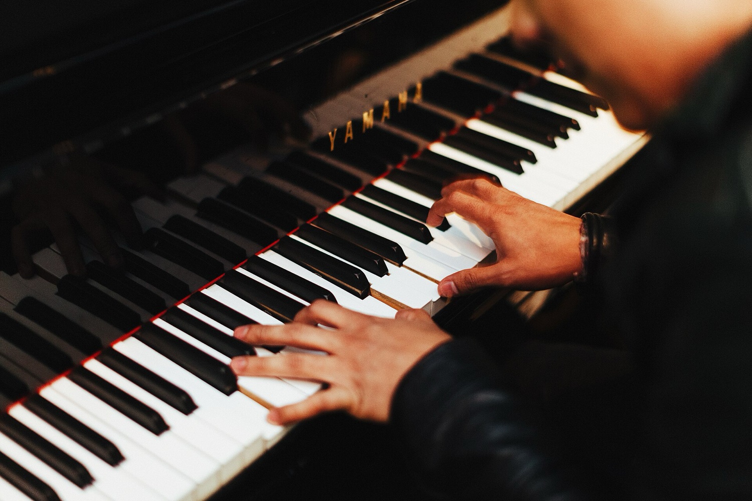 Руки пианиста на клавиатуре рояля Yamaha, крупный план в тёплом свете